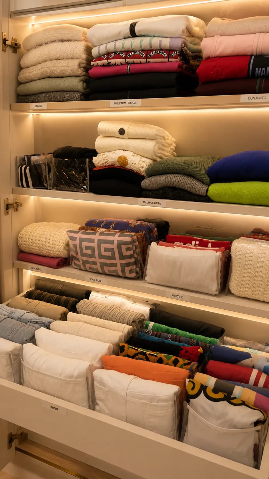 Prateleiras de closet com malhas e suéteres dobrados, etiquetados por categoria e iluminados, Silvana Organizer