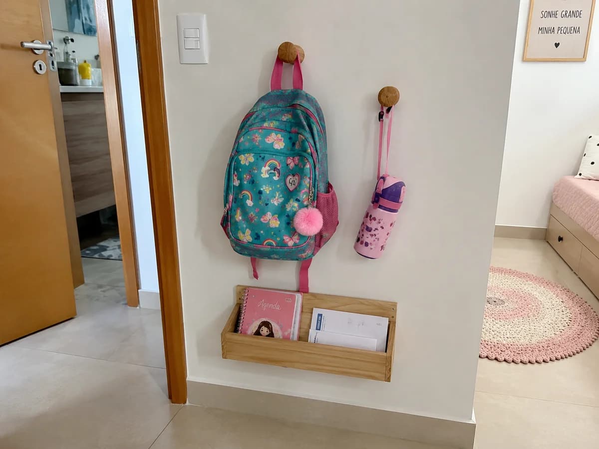 Gancho na parede com mochila escolar e cesto de roupas sujas ao lado, quarto infantil organizado